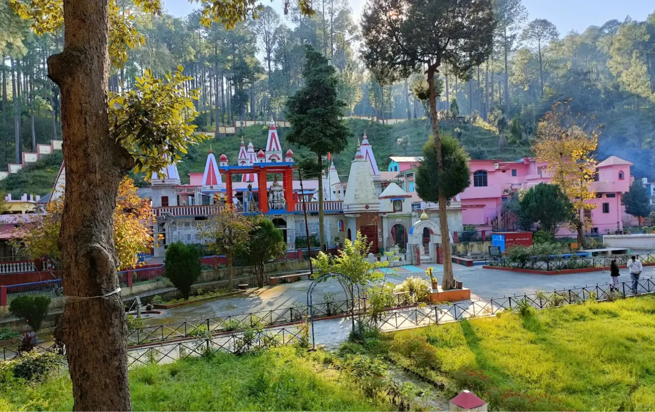 Colourful hillside temple complex with red and white spires surrounded by pine forest near Rankhet, Uttarakhand