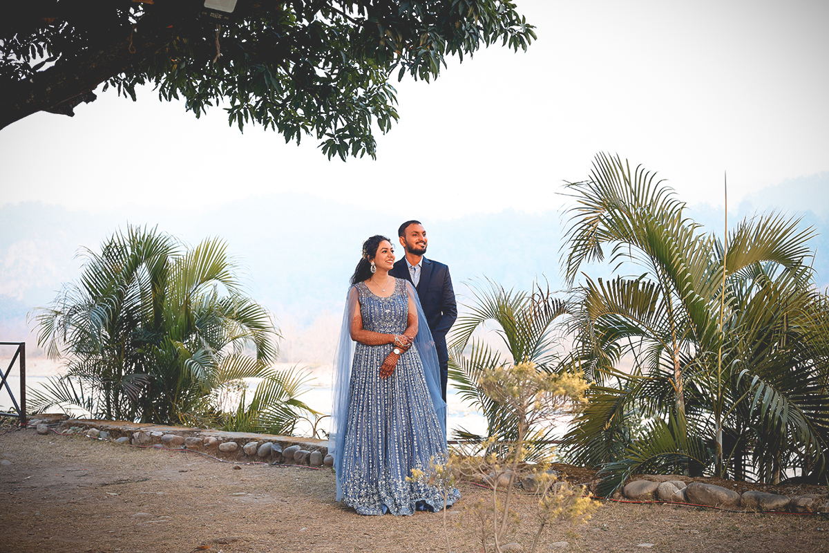 Couple in blue wedding attire among palms with the hills behind them at The Banyan Retreat