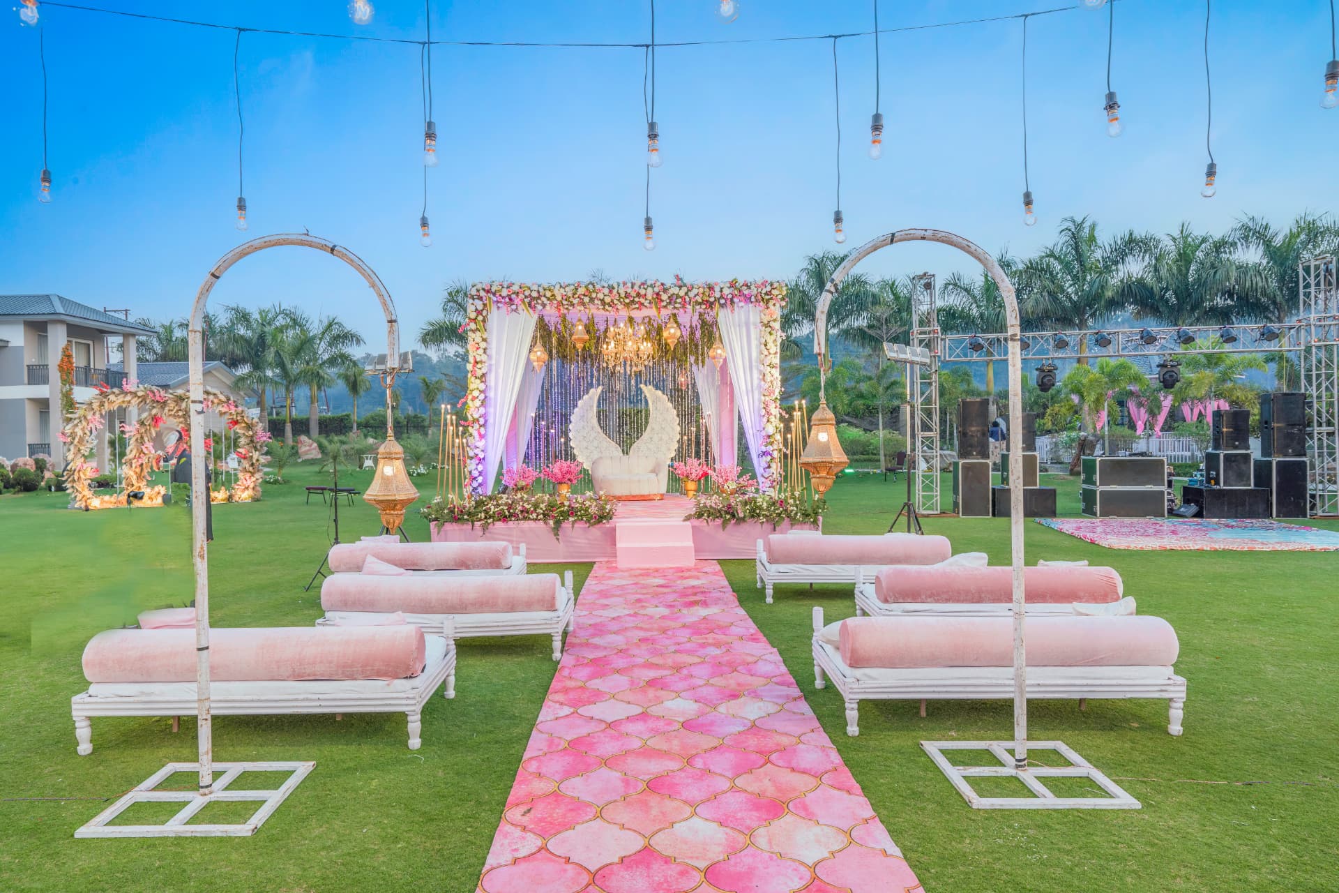 Daytime open-air wedding mandap with white sofas, golden lanterns and a pink aisle at Excel Hotels & Resorts, Corbett