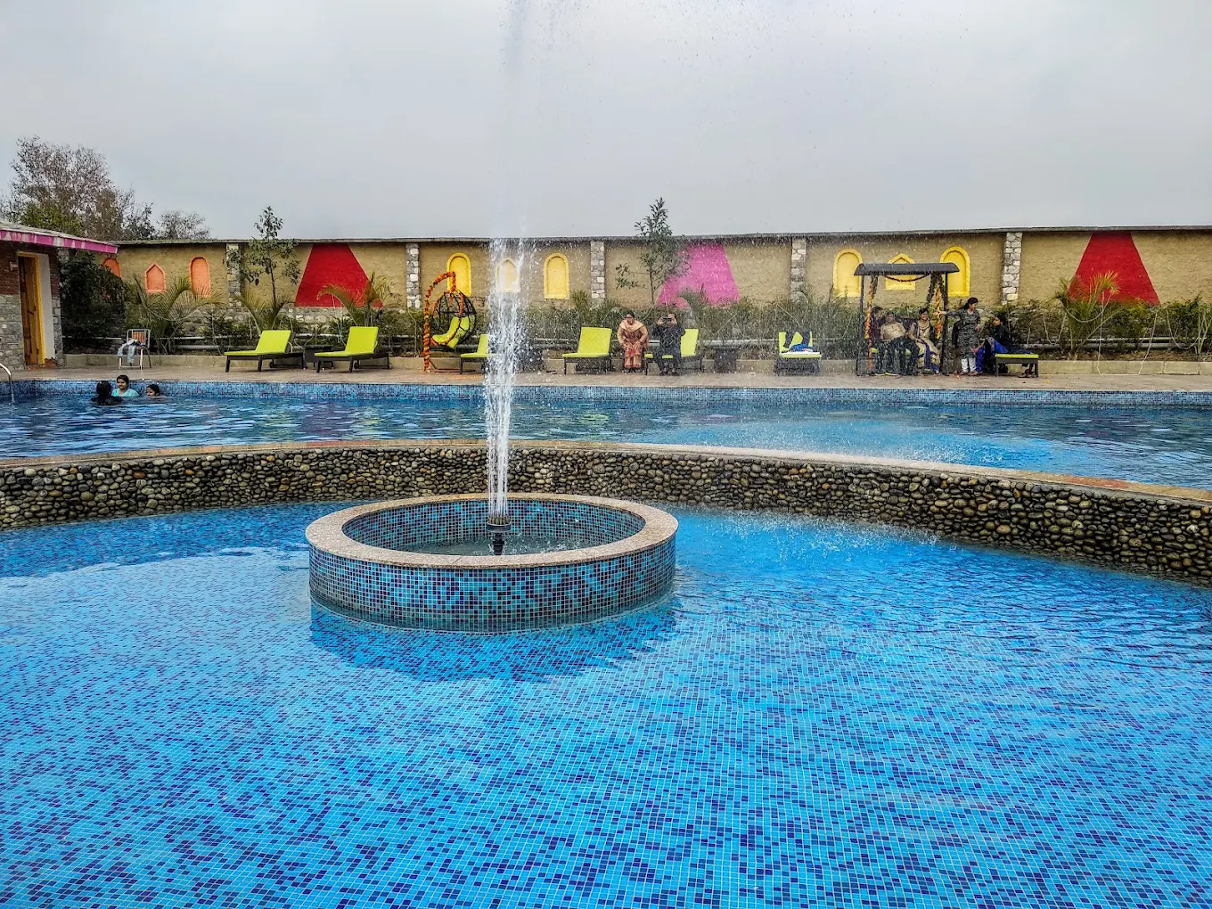 Resort pool with a central fountain, sun loungers and colourful garden cottages