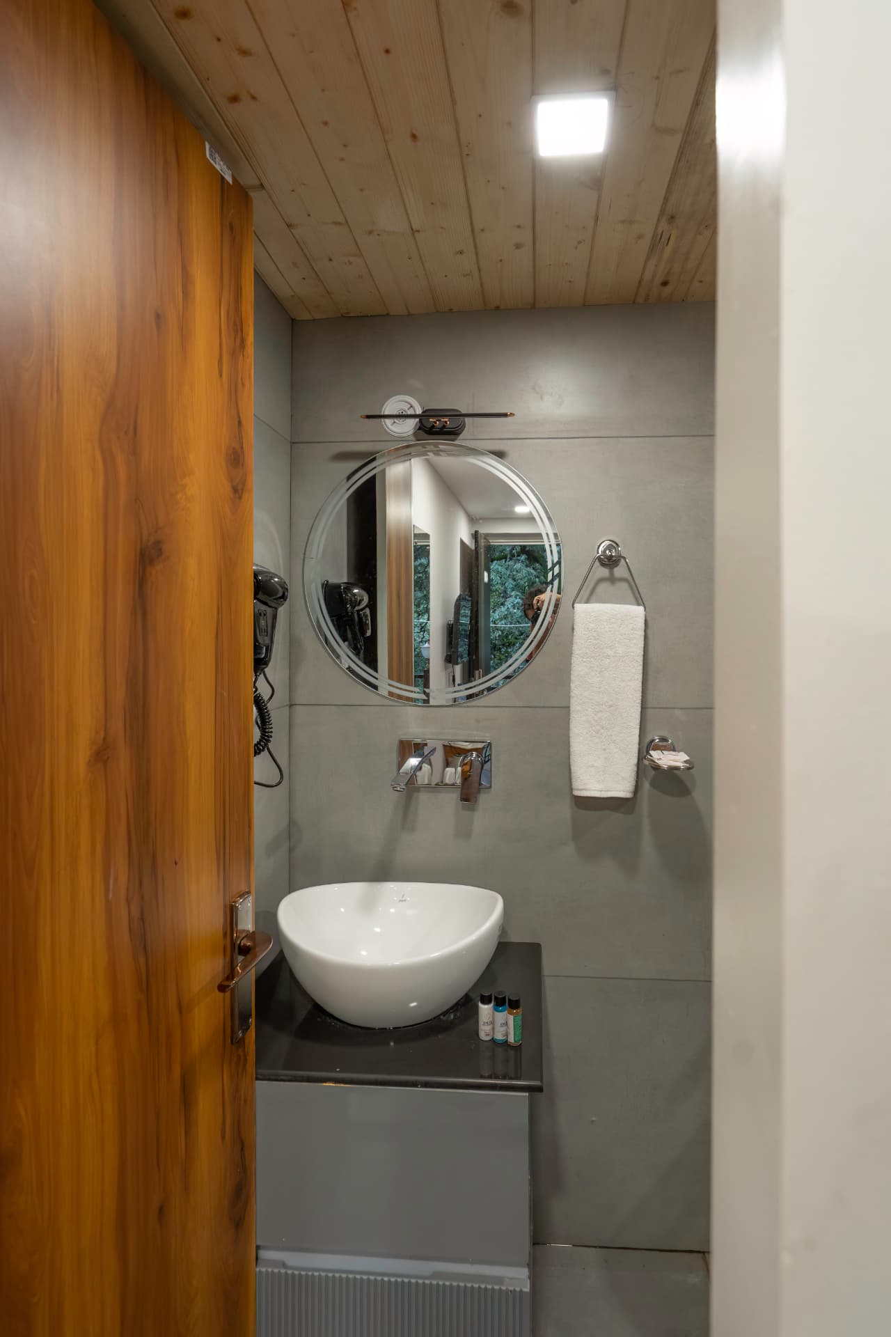 Deluxe Room contemporary bathroom with wooden door, round mirror and premium fixtures