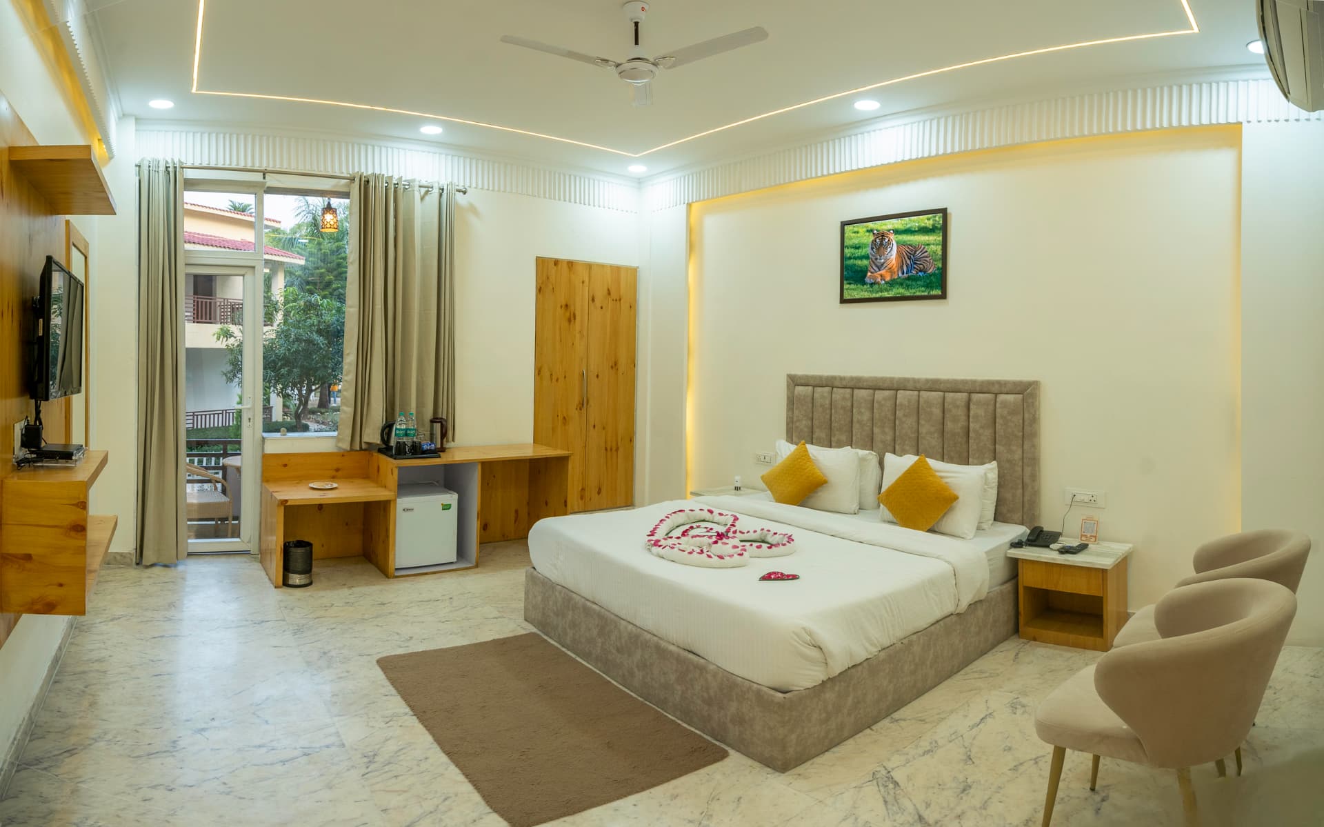 The Oak Room with garden-access balcony door, mini fridge, work desk and tiger artwork at Mango Bloom River Resort