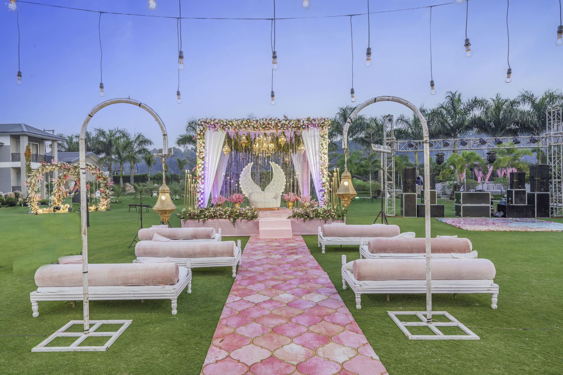 Open-air wedding mandap with white sofas, a pink patterned aisle and golden lanterns at Kotabagh