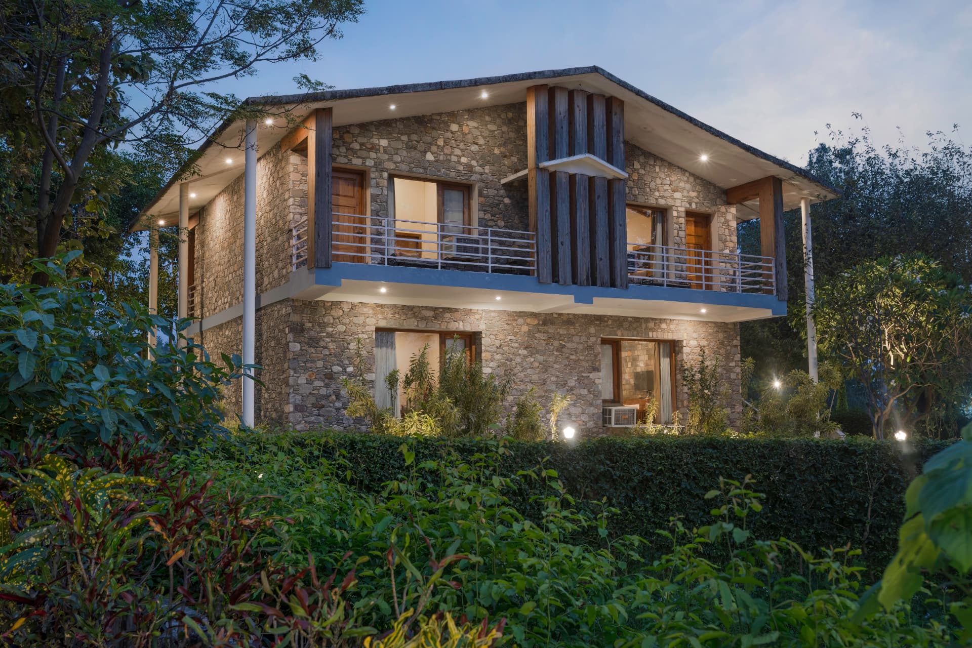 Illuminated stone SplitsVilla building at dusk surrounded by gardens at The Banyan Retreat Corbett