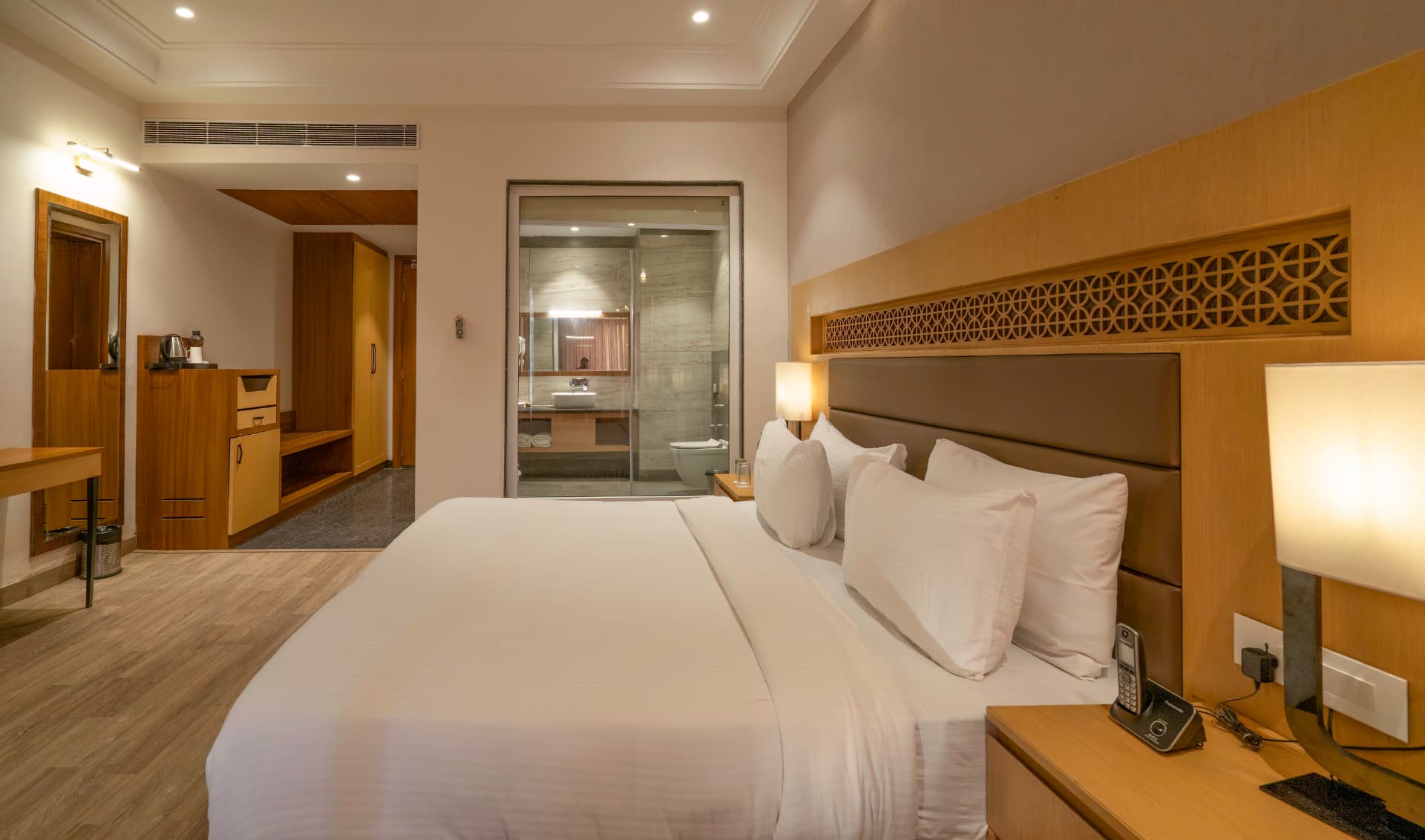 Deluxe Room king bed close-up with glass bathroom and warm lighting at Excel Hotels & Resorts, Kotabagh