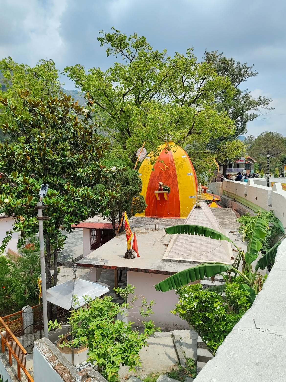 Vibrant orange and yellow shrine surrounded by trees at Bhimeshwar Mahadev Temple