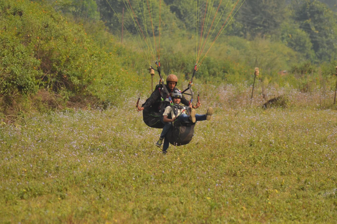 Tandem paraglider coming in to land in a meadow at the Bhimtal adventure park