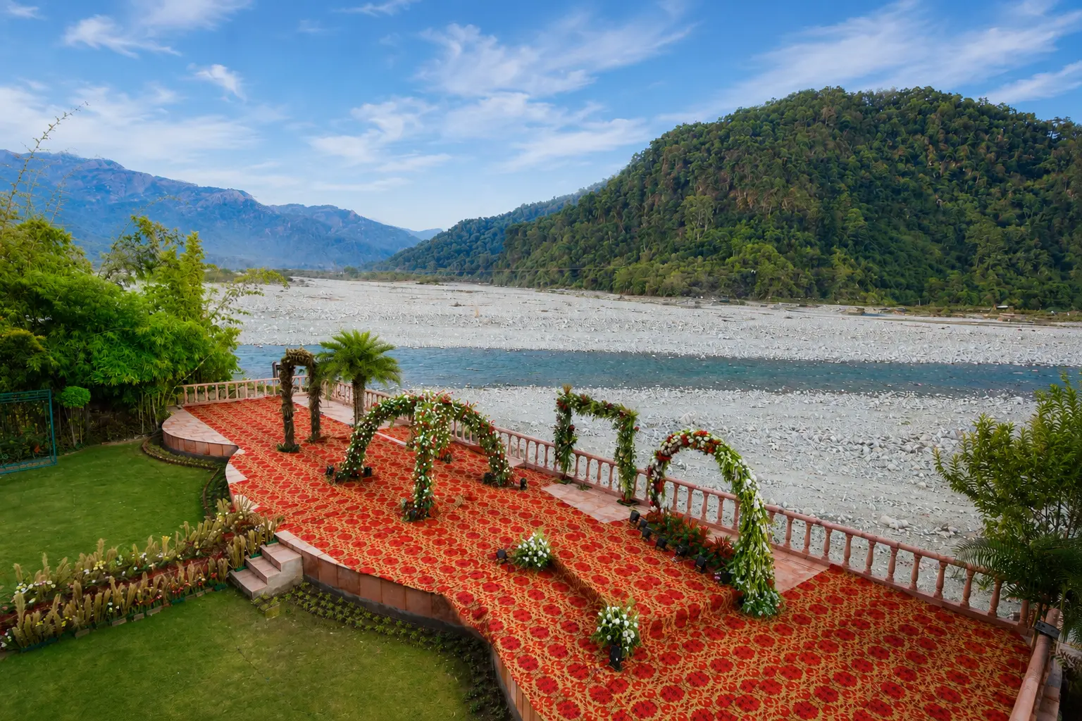Riverside wedding mandap with red carpet and floral arches beside the Kosi River at Mango Bloom