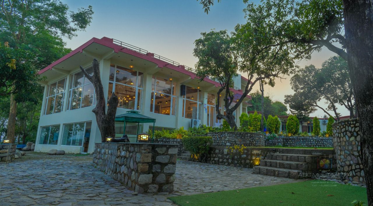 Glass-fronted restaurant building with stone terraces at La Perle River Resort, Jim Corbett