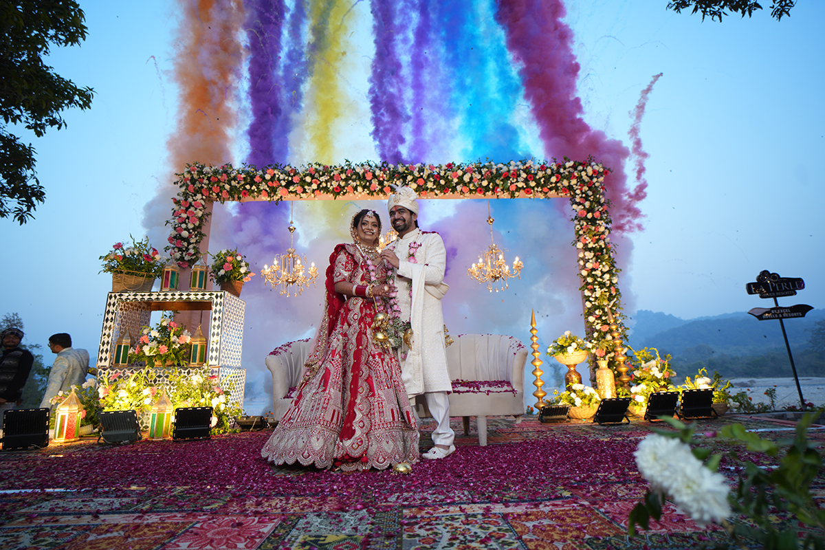 Bride and groom under a floral mandap with colourful smoke at La Perle River Resort