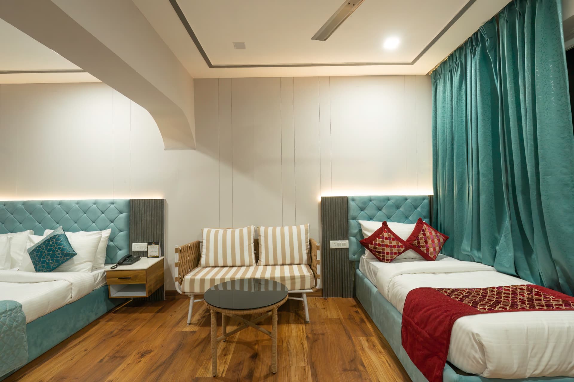 Junior Suite twin-bed arrangement with striped sofa and warm wood flooring at Excel Hotels Nainital