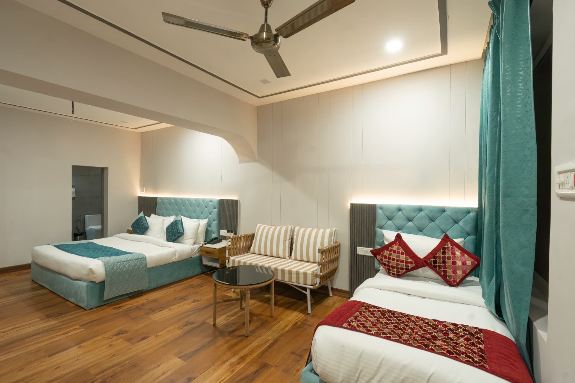 Junior Suite spacious interior with two beds, cane sofa set and teal accents at Excel Hotels Nainital