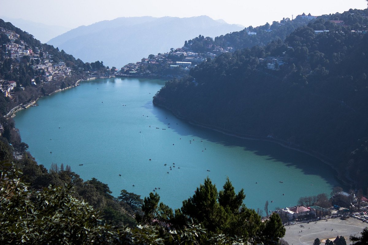 Naini Lake and Nainital town seen from above, with boats on the water and forested hills