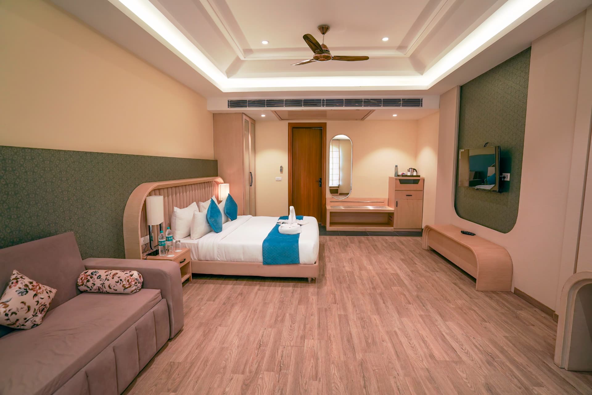Premium Room interior with king bed, sofa, green accent wall and wooden flooring at Excel Hotels & Resorts, Kotabagh